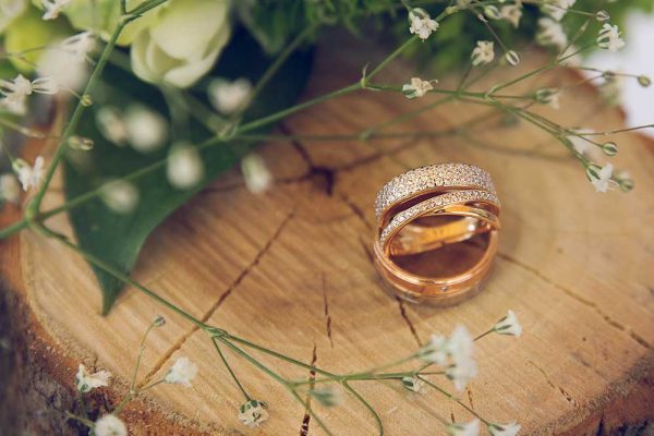 Two wedding rings with diamonds on wooden stump with dahlias and gypsophilas